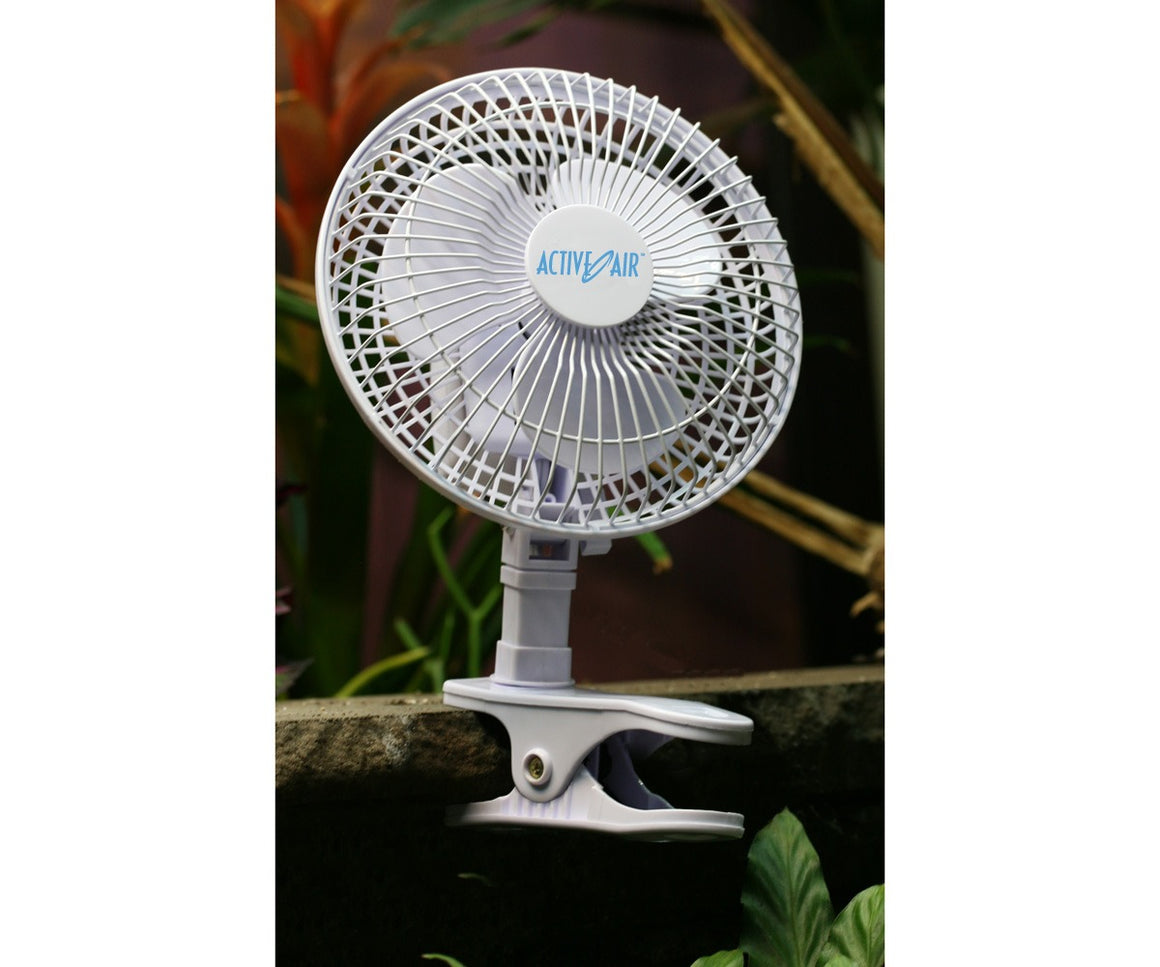 White Active Air clip-on fan attached to a stone ledge, with blurred green foliage in the background.