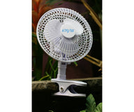 White Active Air clip-on fan attached to a stone ledge, with blurred green foliage in the background.