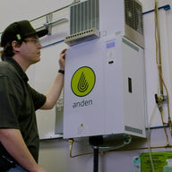 Man in a cap inspects a white Anden steam humidifier unit mounted on a wall.