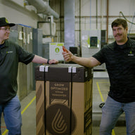 Two men stand by a large cardboard box labeled 