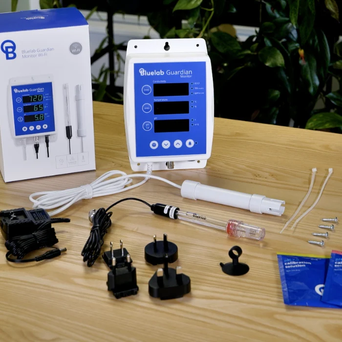 BlueLab Guardian Monitor Wi-Fi with probes, power adapters, and calibration solutions on a wooden table.