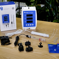 BlueLab Guardian Monitor Wi-Fi with probes, power adapters, and calibration solutions on a wooden table.