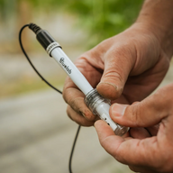 A person holds a white Bluelab soil pH probe with a black cable.