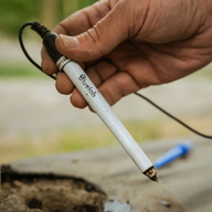A hand holds a Bluelab soil pH probe near dirt.