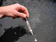 A hand holds a Bluelab pH probe in dark, bubbly water.