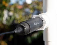 Bluelab pH probe attached to white pipe, with blurry greenery background.