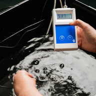 Hand holds Bluelab ORP meter displaying 537mV above bubbling dark water.
