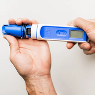 Hands hold a blue and white Bluelab OnePen pH tester with a digital display.