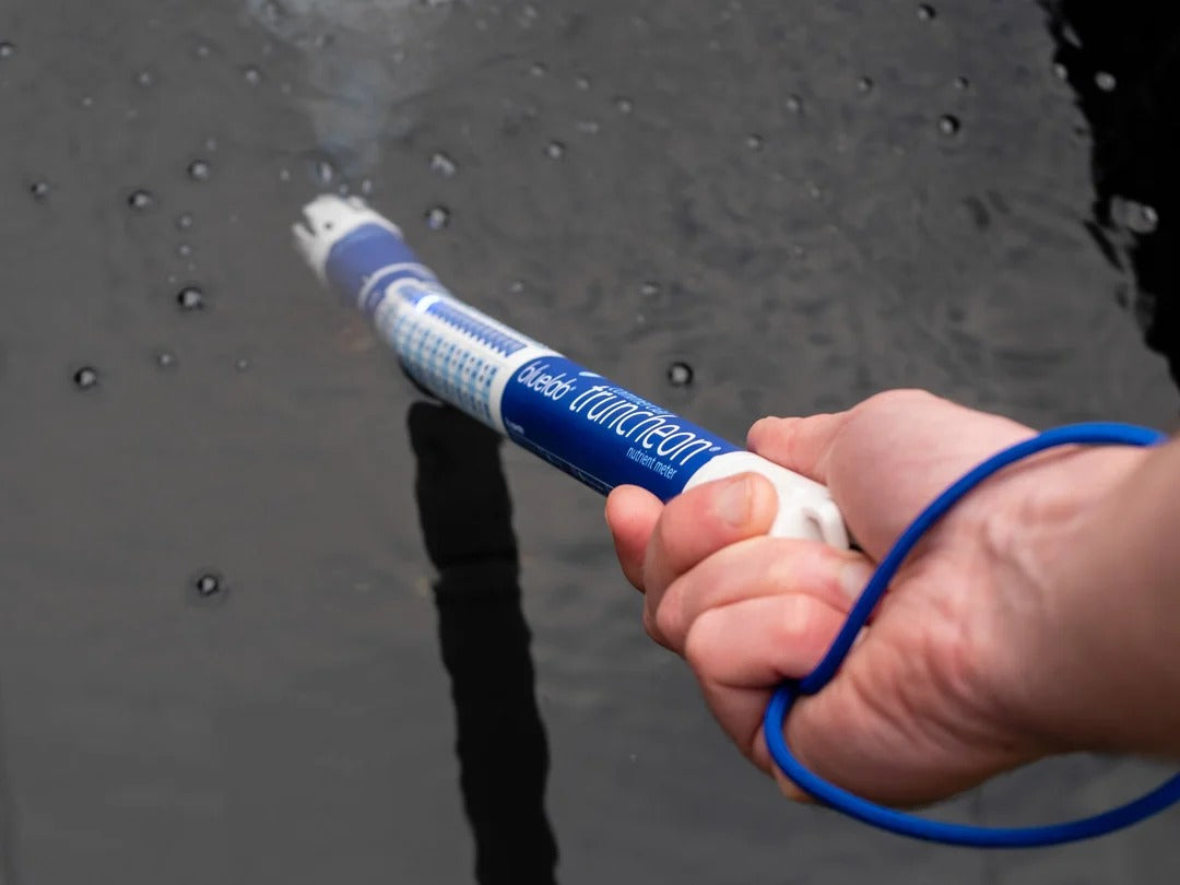 Hand holding Bluelab Truncheon nutrient meter in dark water with bubbles.