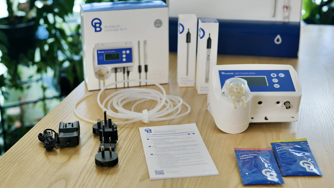 Bluelab pH Controller Wi-Fi kit with probes, tubes, power adapter, and calibration solutions on a wooden table.
