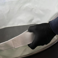 Black gloved hand holds white strap of large open laundry bag.