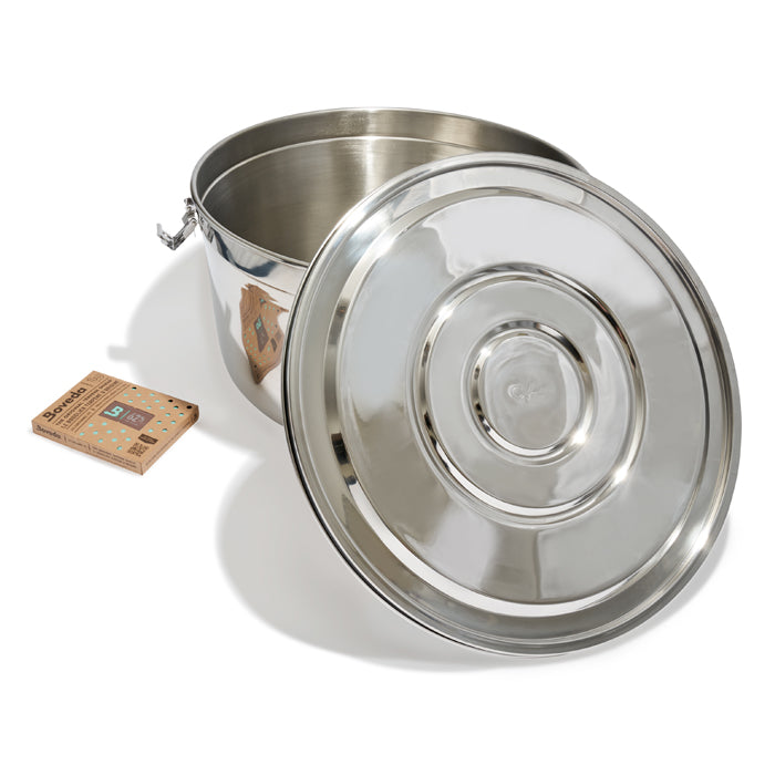 Stainless steel CVault storage container with lid open, next to Boveda humidity pack.