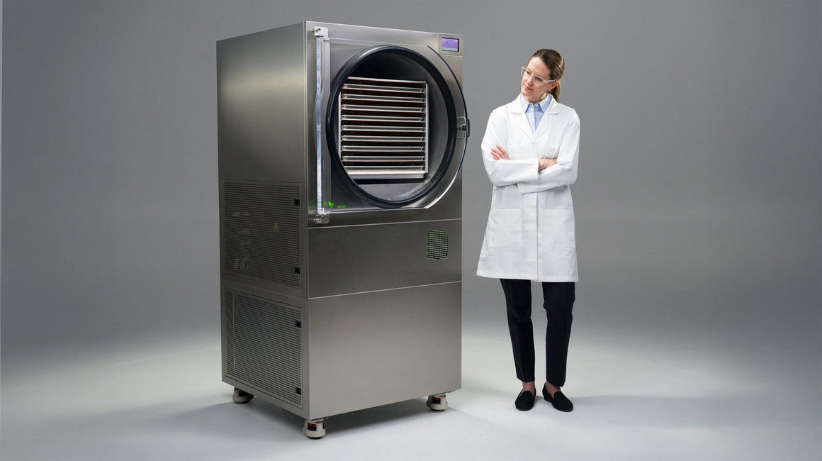 Woman in lab coat stands next to large freeze dryer with open door.