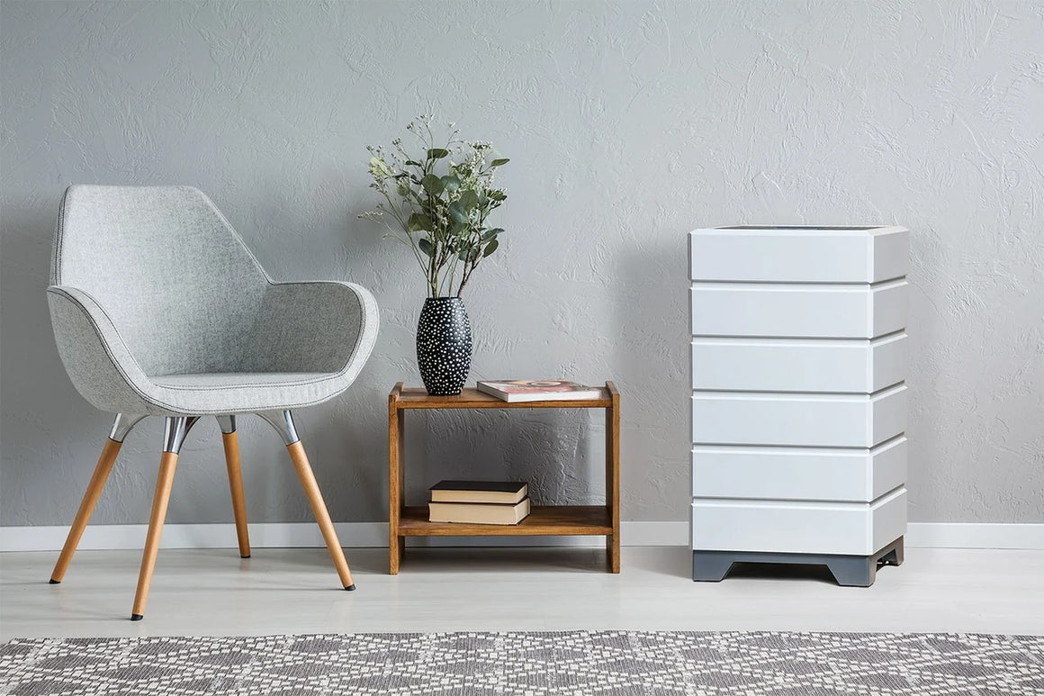 Modern gray chair, wooden side table with books and vase, and a white air purifier next to a textured gray wall.