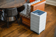 White Aspen air purifier with blue gridded top, next to wood booth seating and a round dining table.