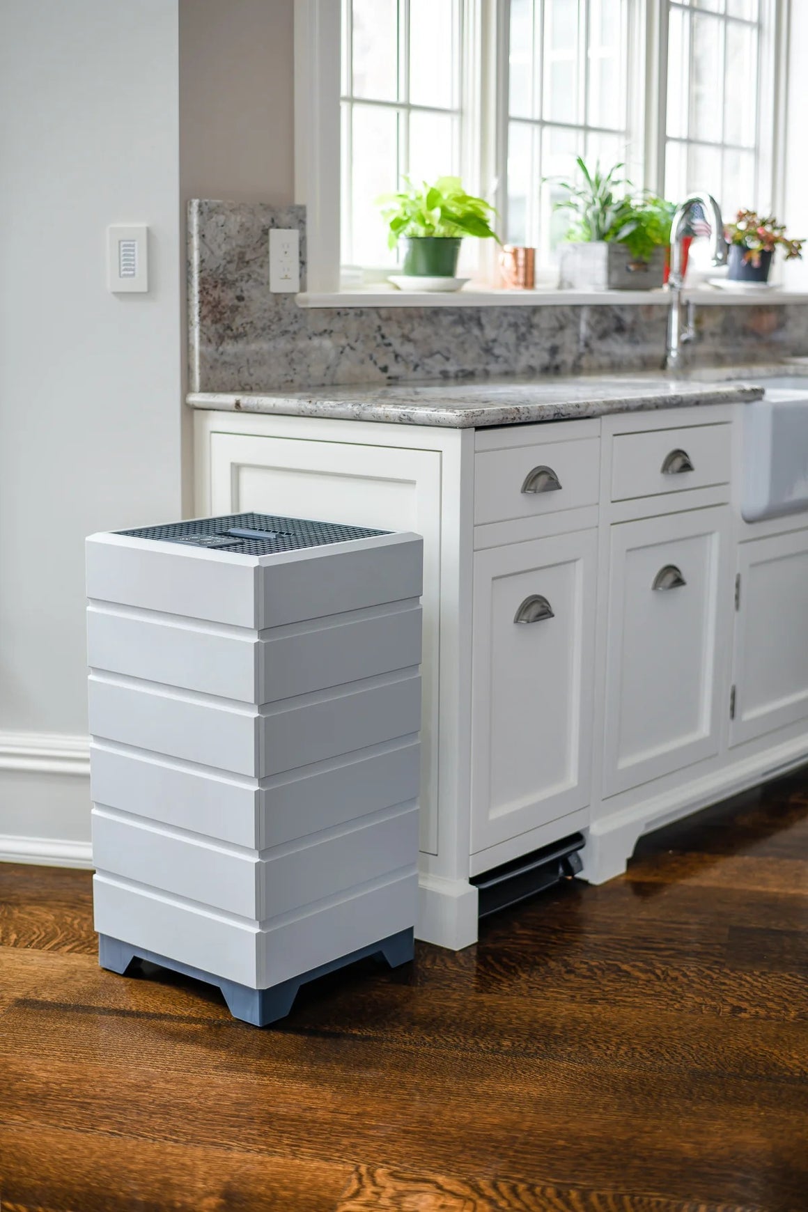White stacked air purifier with grey top next to white kitchen cabinets and a granite countertop.