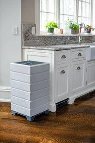 White stacked air purifier with grey top next to white kitchen cabinets and a granite countertop.