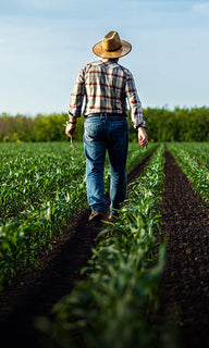 Farmer in straw hat and plaid shirt walks through a green field.