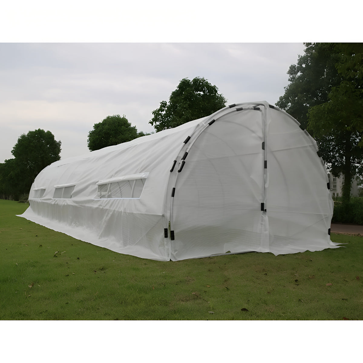 White hoop house greenhouse with roll-up windows on grassy field.