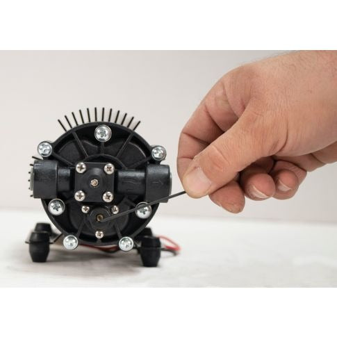 Close-up of a hand adjusting a black diaphragm pump with a black wire.