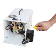A hand uses a yellow-handled screwdriver to adjust a white booster pump with a brass component.