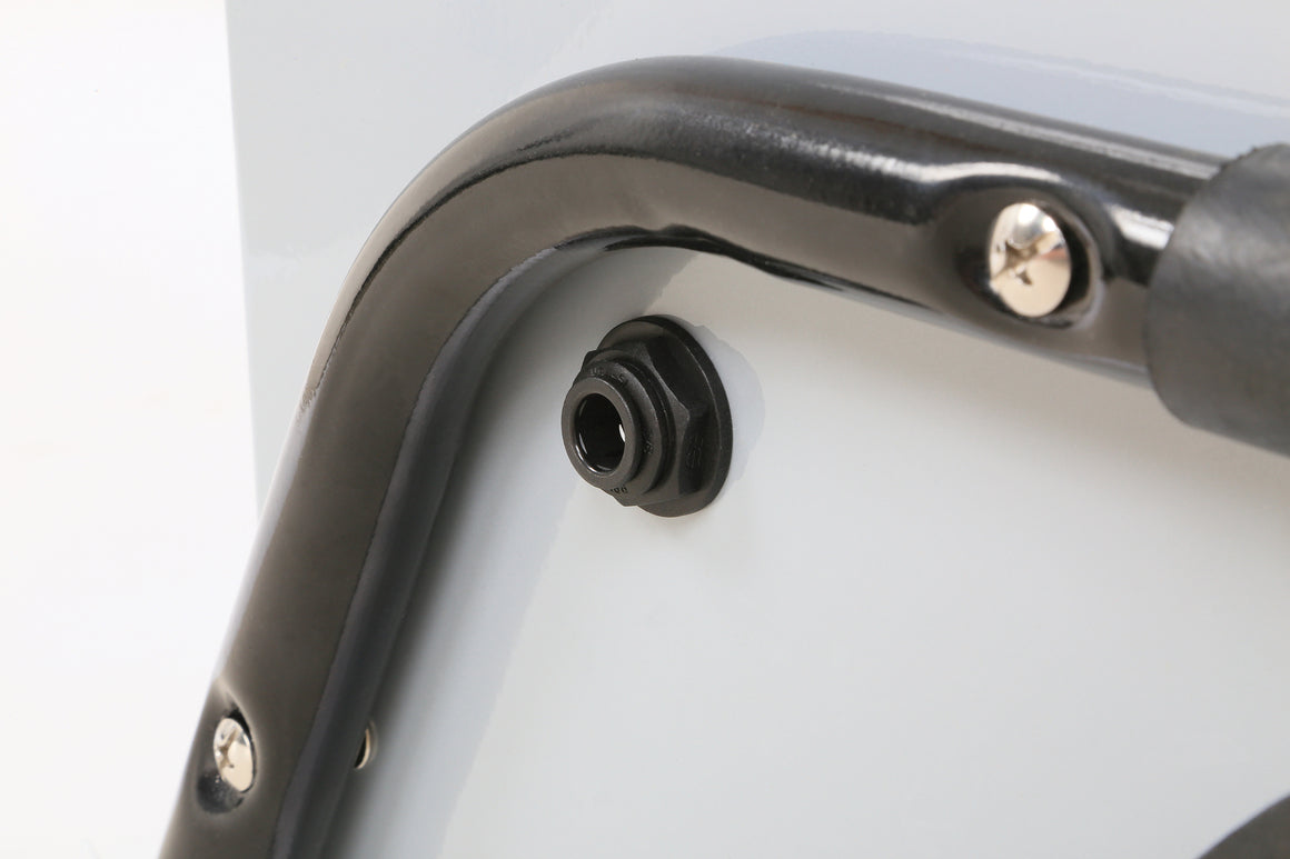 Close-up of a black hex nut with a white washer on a gray surface next to a shiny black metal bar.