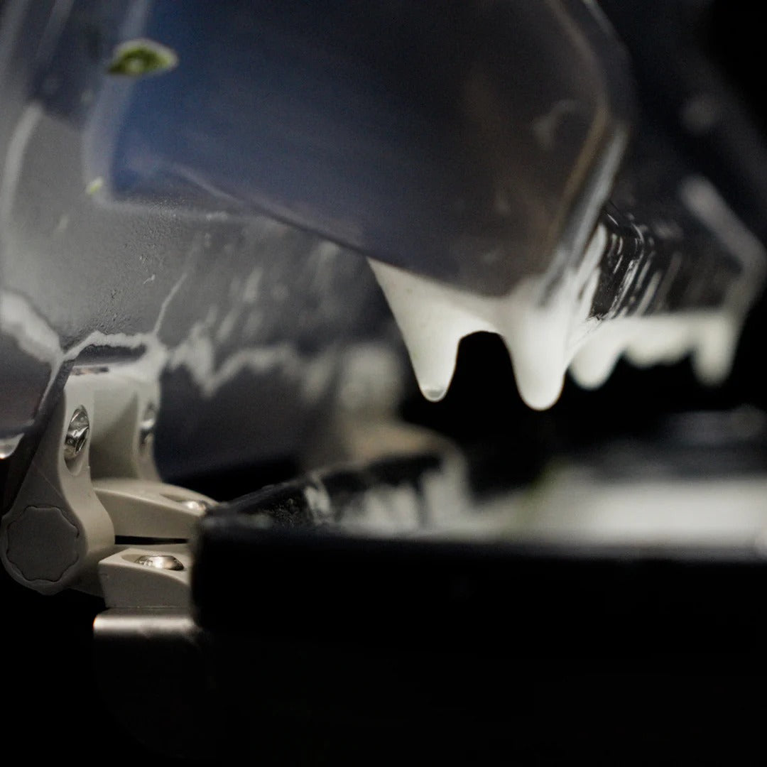 Close-up of white foam dripping from a dark metal component onto a black surface.