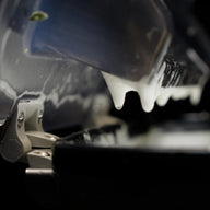 Close-up of white foam dripping from a dark metal component onto a black surface.