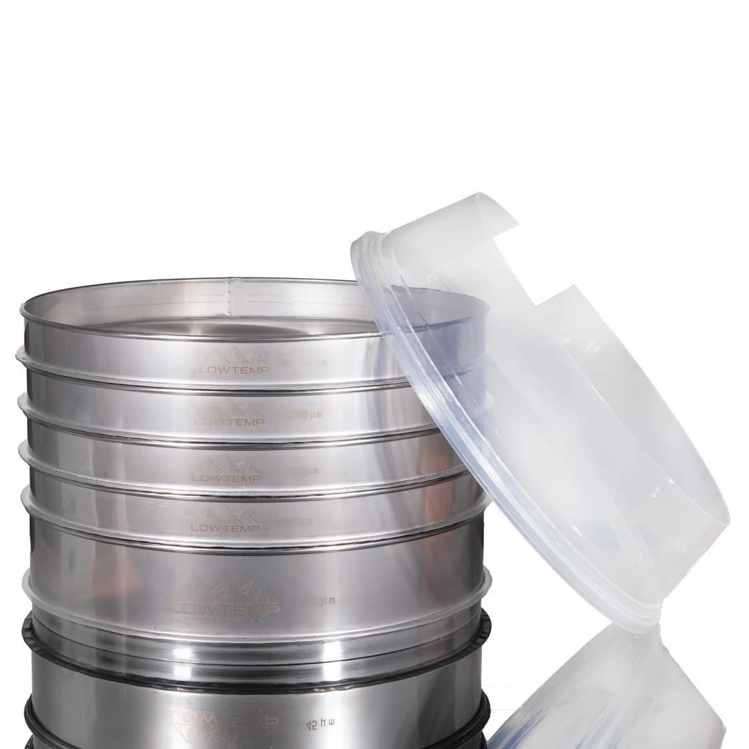 Stack of stainless steel sieves with a clear plastic lid for soil analysis or laboratory use.