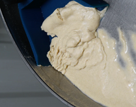 A blue spatula scrapes beige batter from a metal bowl, showing smooth and textured batter.