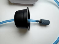 Black cone-shaped fitting connected to blue airline tubing with an aeration stone, on textured white surface.