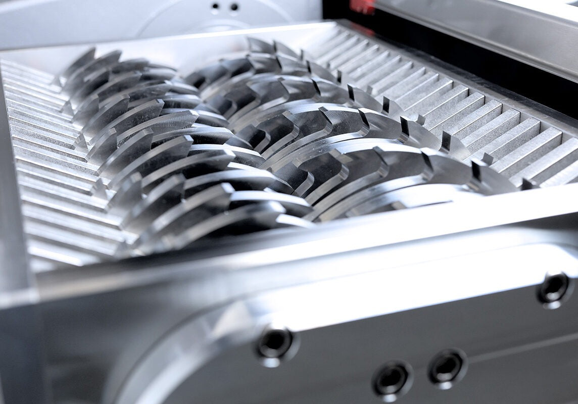 Close-up of a shredder's sharp, interlocking metal blades in a metallic housing.