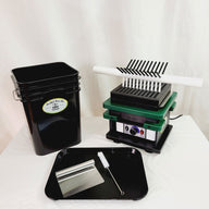 Black bucket, capsule filler machine, scraper, and brush on a white surface.