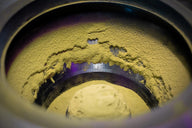 Yellow powder fills a metal container, with purple light reflecting off the sides.