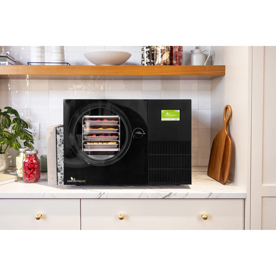 Black Countertop 360 freeze dryer on a white counter under open wooden shelves with jars of freeze-dried food