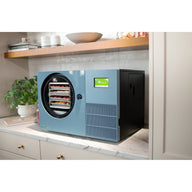 Pale blue Countertop 360 freeze dryer on a marble counter next to a potted plant and a wooden cutting board
