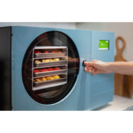 Hand turning the door latch of the pale blue Countertop 360, with trays of fruit visible through the round window
