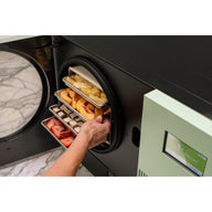 Hand sliding out trays of peaches, chocolate pieces and strawberries from the sage green Countertop 360 on a marble counter