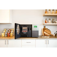 Stainless steel Countertop 360 freeze dryer with its door open on a butcher-block counter among jars of freeze-dried food