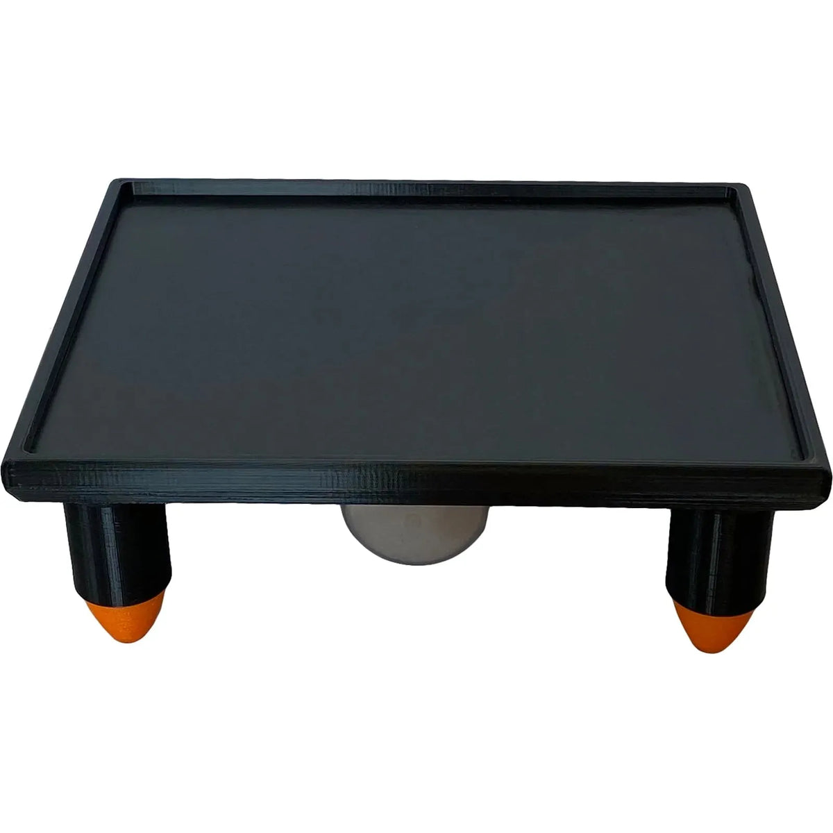 Black rectangular vibration table with raised edges, four black legs, orange feet, and a white vibrator underneath.