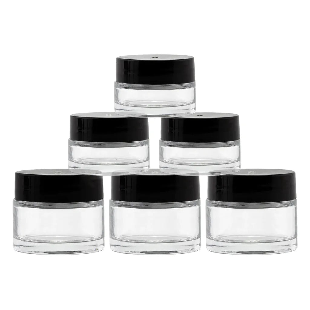Six small, clear glass jars with black lids are arranged in a pyramid shape.